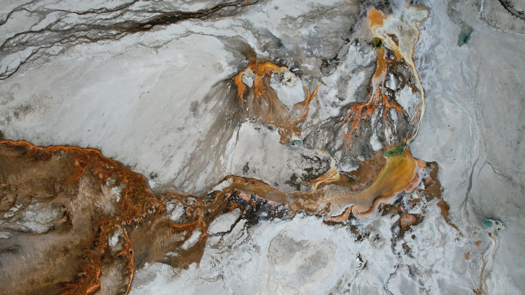 Aerial view of mineral terraces and hot-spring channels in orange and white.